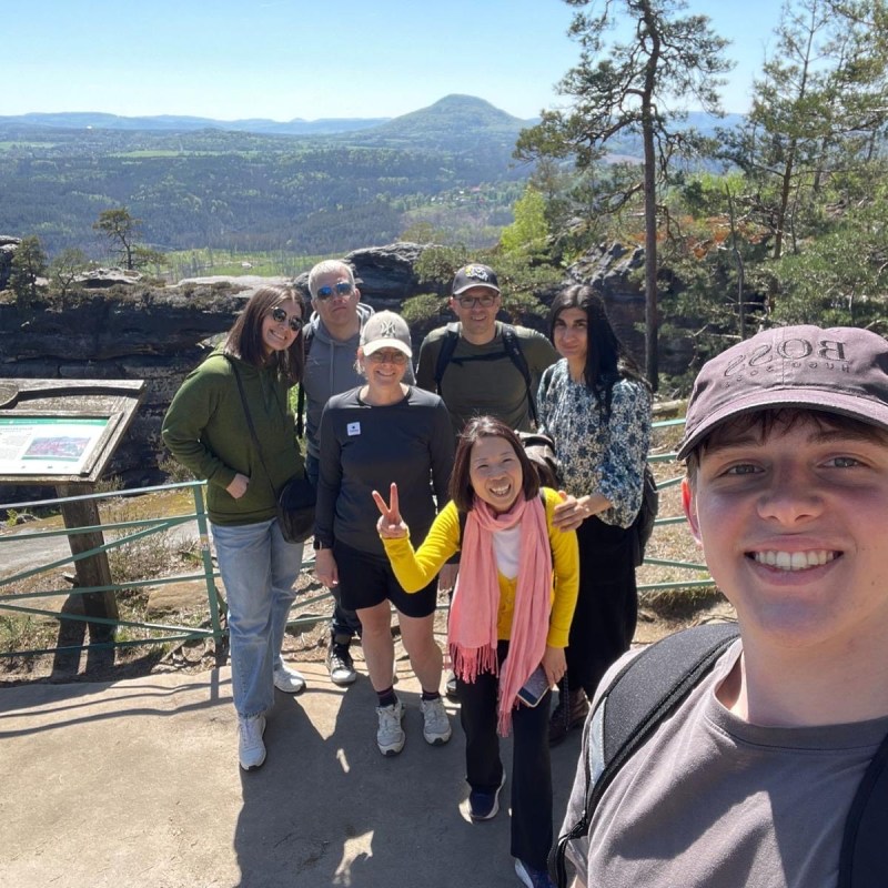 Group of seven people posing for a photo on a scenic overlook with mountains and trees in the background.