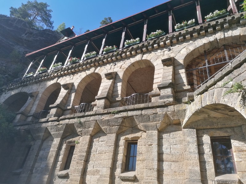 Stone building with arches and flower boxes, set against a rocky cliff.