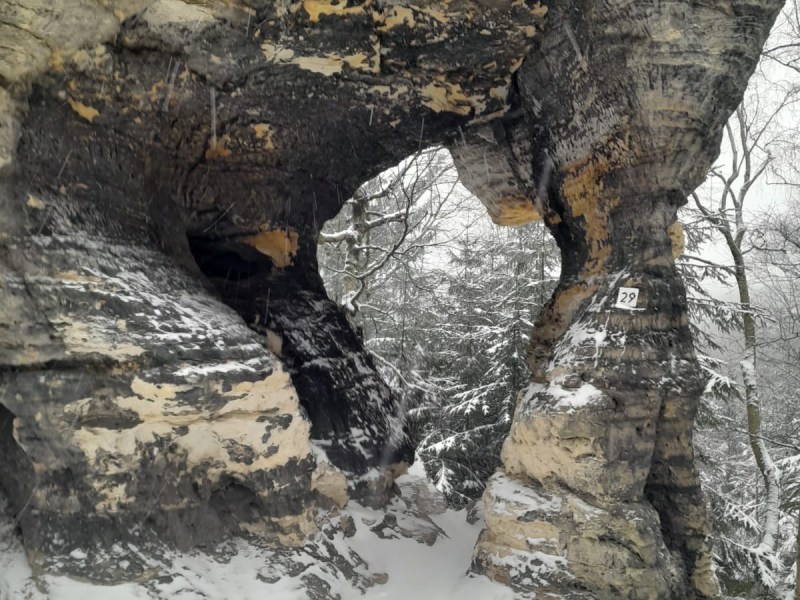 Snow-covered rocky arch with a forest backdrop on a winter day.