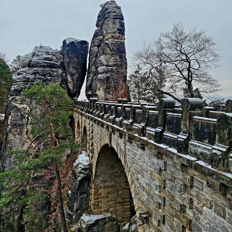 Stone bridge with archways and tall rock formations on a cloudy day.