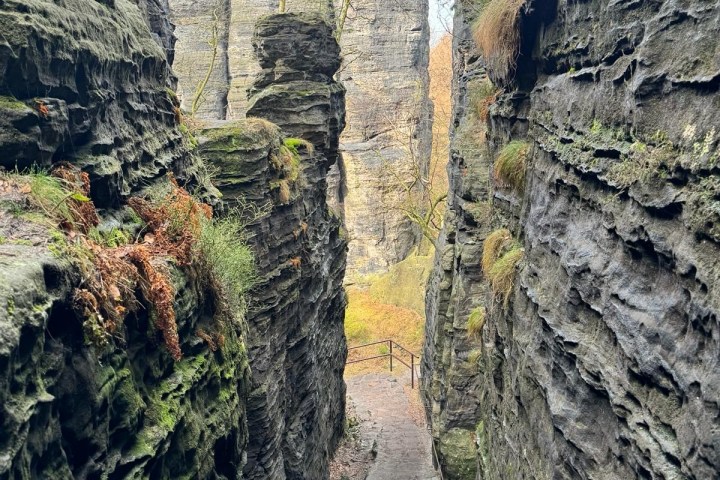 Narrow stone path between tall rock formations with sparse vegetation and railing.
