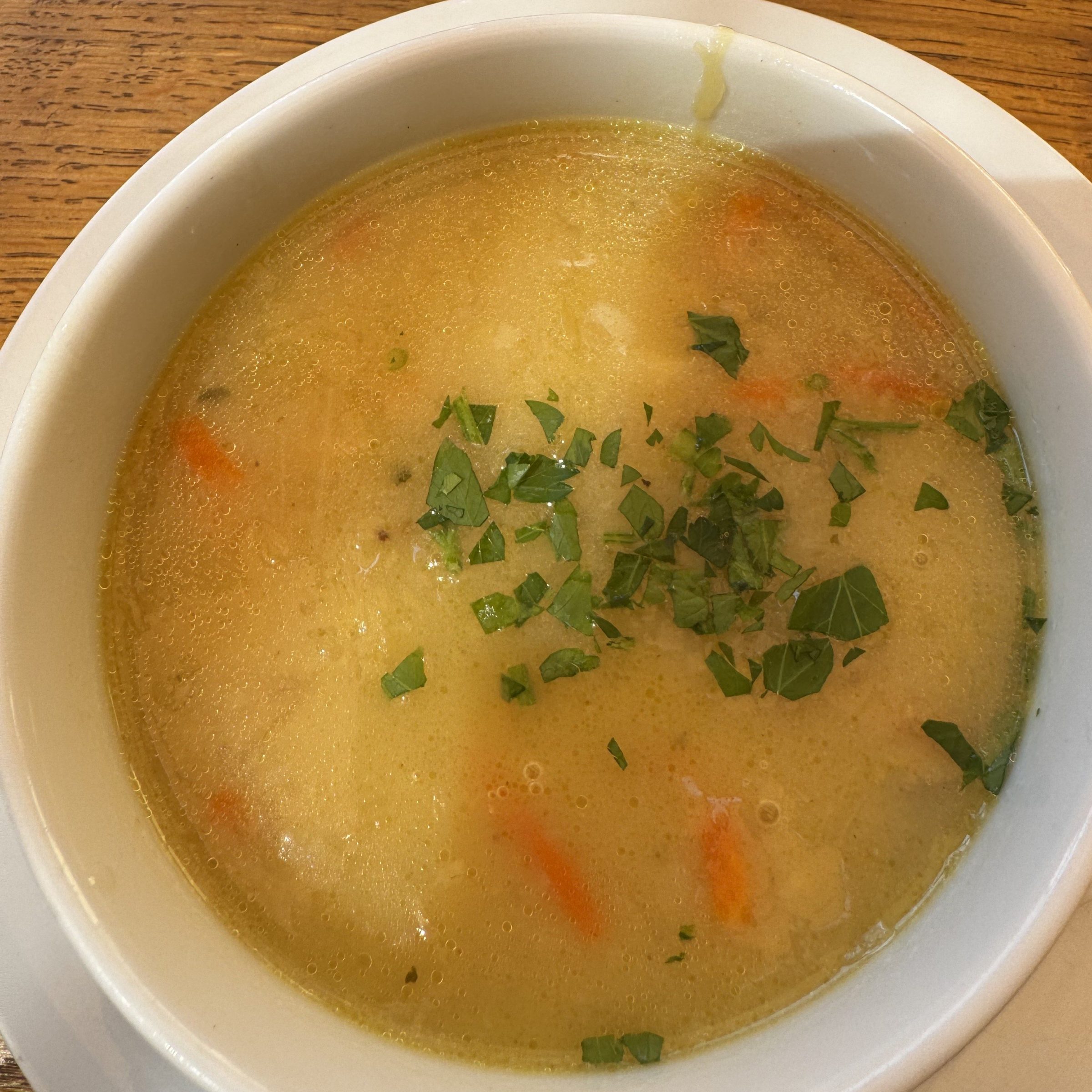 A bowl of soup garnished with chopped herbs on a wooden table.
