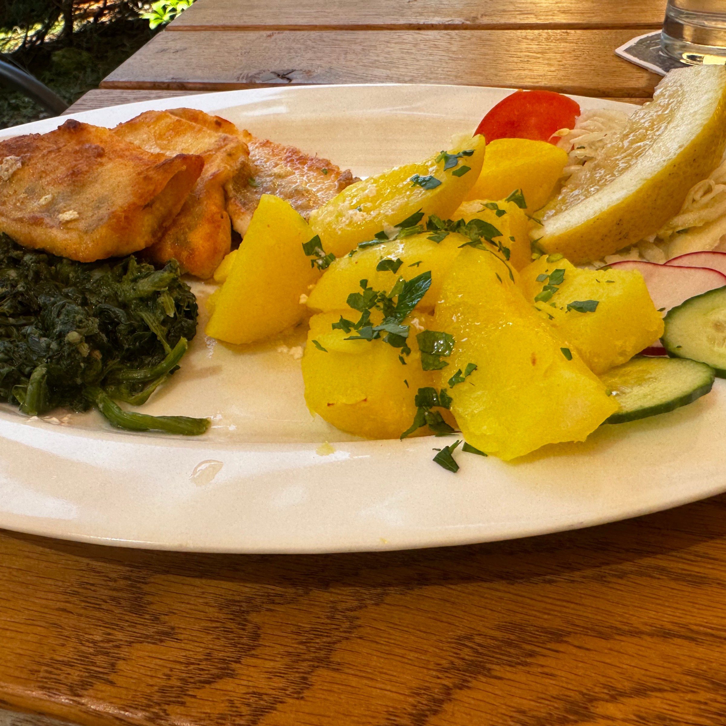Plate with fish, spinach, potatoes, lemon wedge, and sliced cucumber and radish on a wooden table.