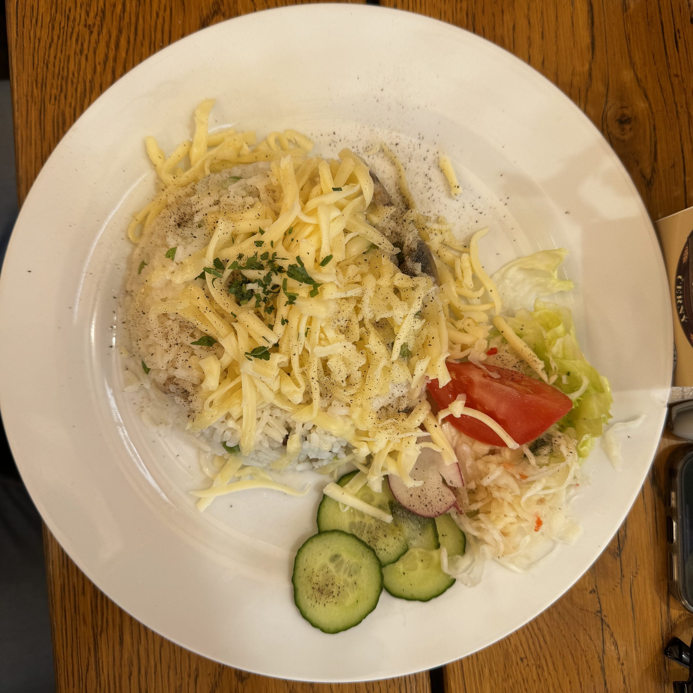 Plate with rice, melted cheese, and mixed salad with cucumber and tomato on a wooden table.