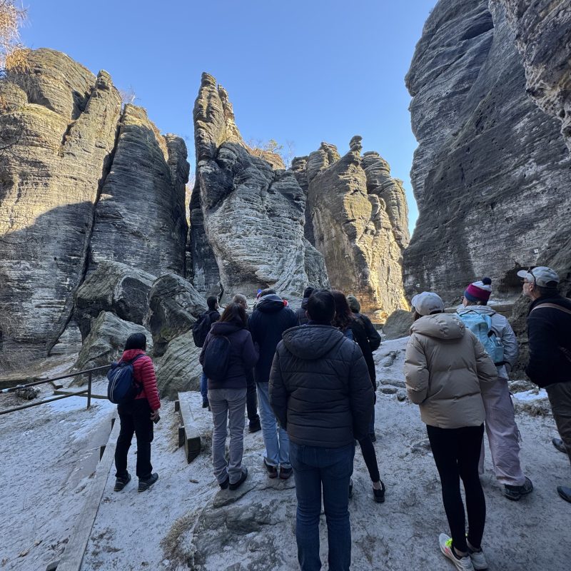 People hiking through a narrow rocky canyon with clear blue sky above.