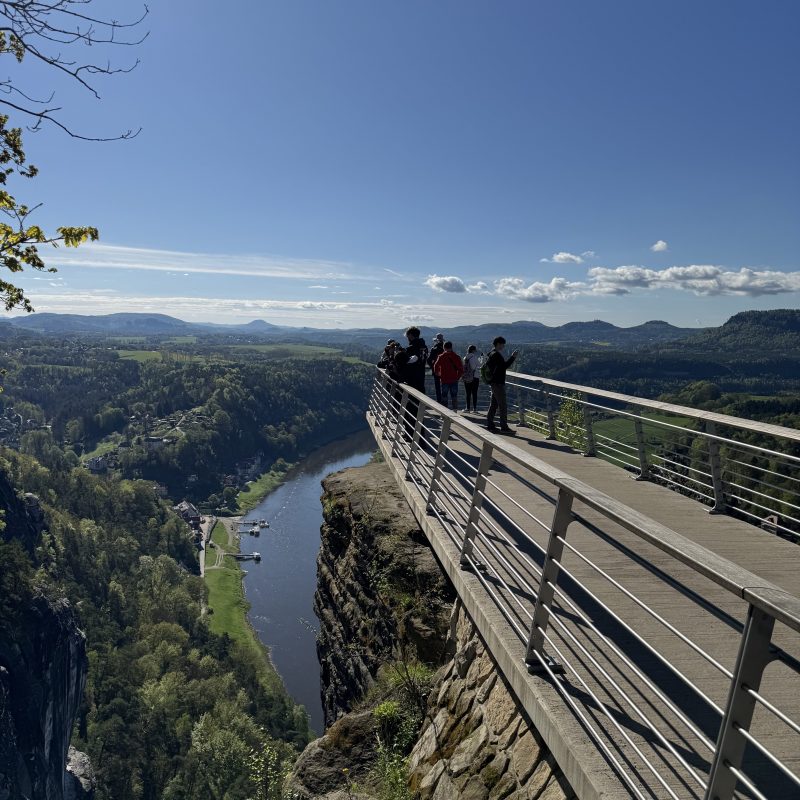 Group of people on a lookout platform with a river and forested valley below.