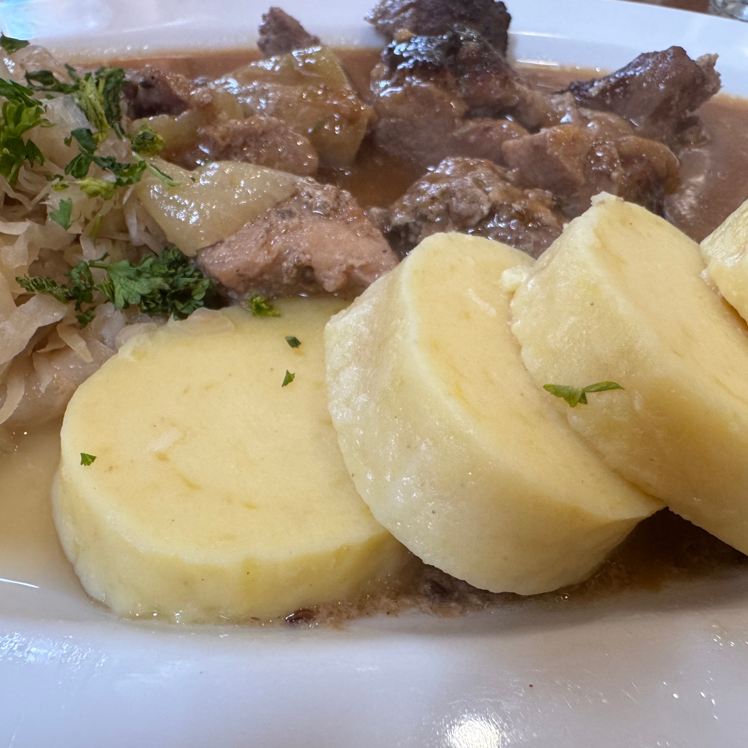Plate of dumplings, sauerkraut, and meat with gravy.