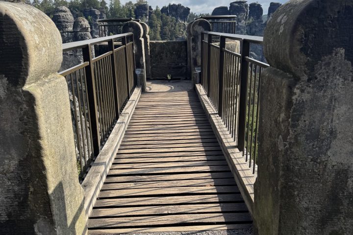 Stone bridge with wooden walkway and railings, overlooking rocky landscape under cloudy sky.