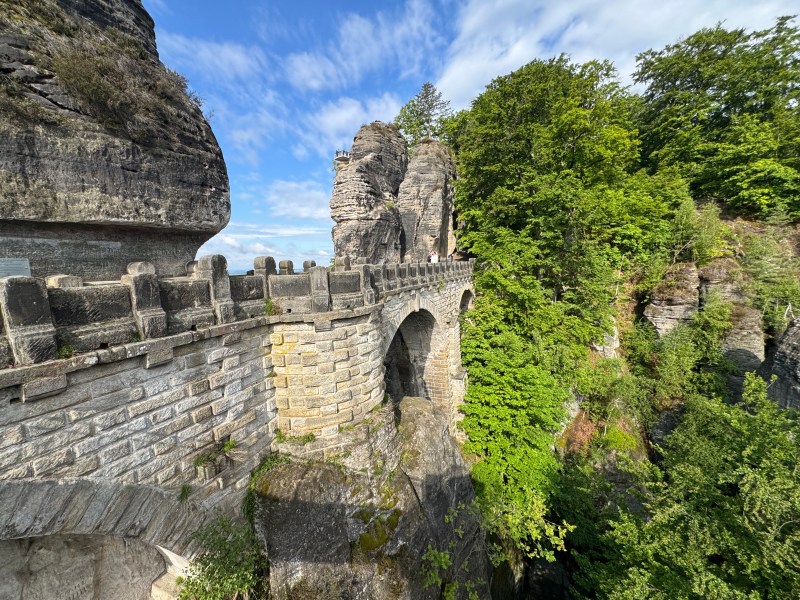 Stone bridge over rocky gorge with green trees on a sunny day.