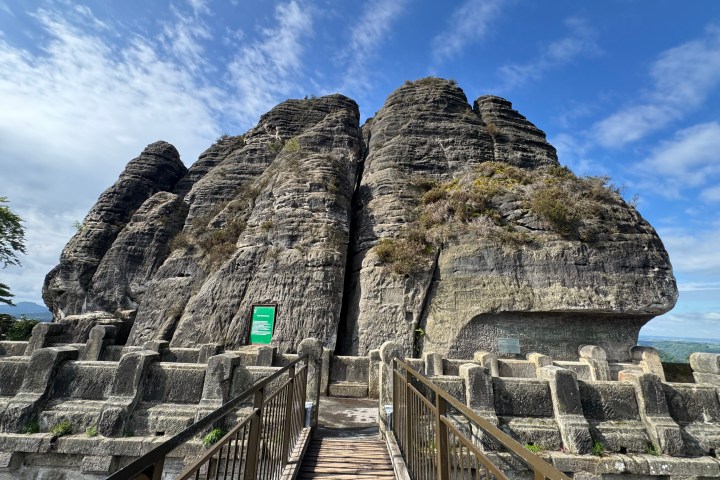 Stone cliff with metal railing walkway under a blue sky.