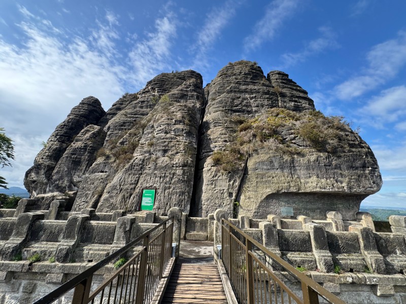 Stone cliff with metal railing walkway under a blue sky.