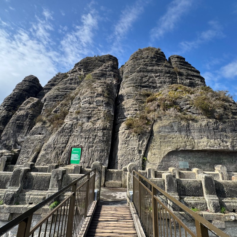 Stone cliff with metal railing walkway under a blue sky.