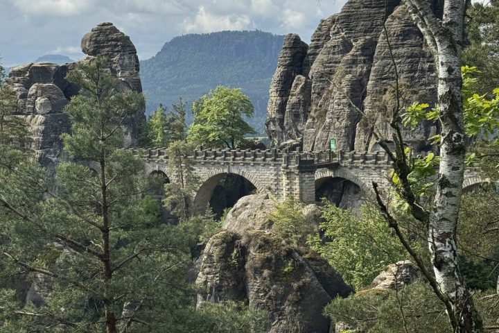 Stone bridge amidst tall rock formations and trees under a cloudy sky.