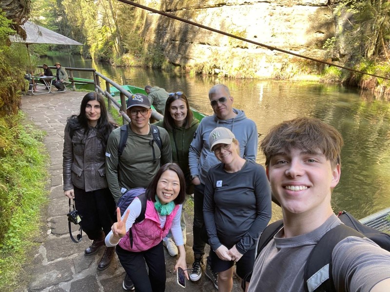 Group of seven people posing near a river with a rocky background on a sunny day.
