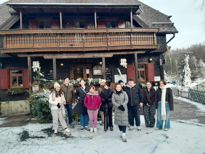 Group of people standing in front of a wooden chalet in a snowy landscape.