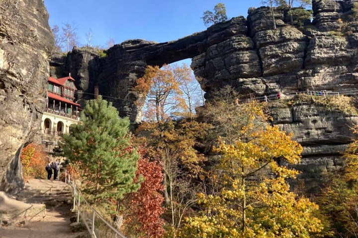 Majestic rocky arch and autumn foliage with a path and building in the background.