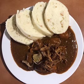 Plate with sliced dumplings and goulash with onions on a brown sauce.