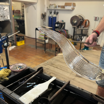 Person holding a curved, partially made glass object in a workshop setting.
