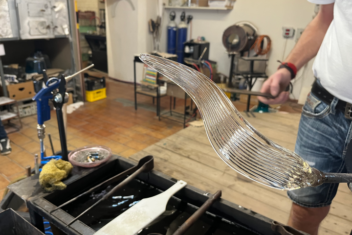 Person holding a curved, partially made glass object in a workshop setting.