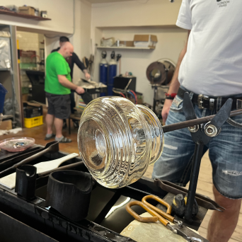 Person shaping glass with tools in a workshop, wearing casual clothes.