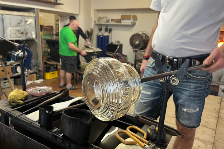 Person shaping glass with tools in a workshop, wearing casual clothes.