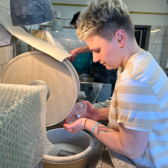 Person polishing a glass object at a workshop with a grinding wheel.