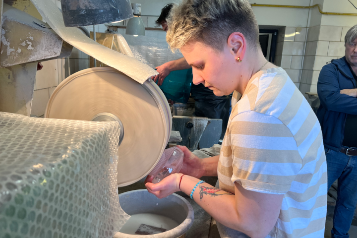 Person polishing a glass object at a workshop with a grinding wheel.