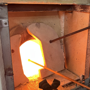 Open furnace with bright orange glow heating a metal rod.