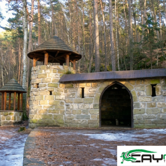 Stone building with pointed towers in a forest, light snow on the ground.