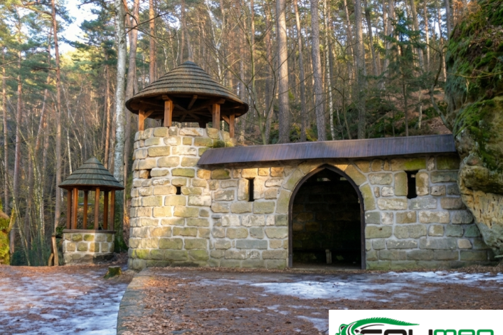 Stone building with pointed towers in a forest, light snow on the ground.