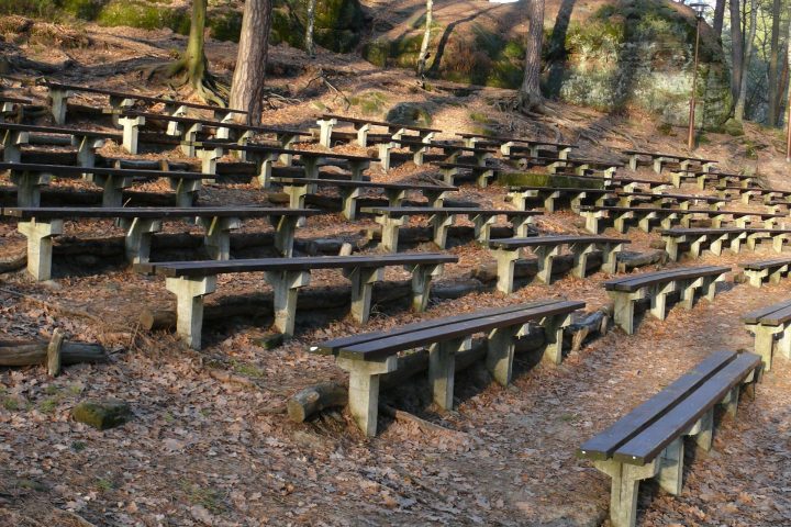 Outdoor amphitheater with wooden benches surrounded by trees and rocky terrain.