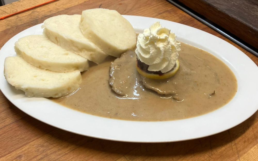 Plate of bread dumplings with meat in gravy and whipped cream on a lemon slice.