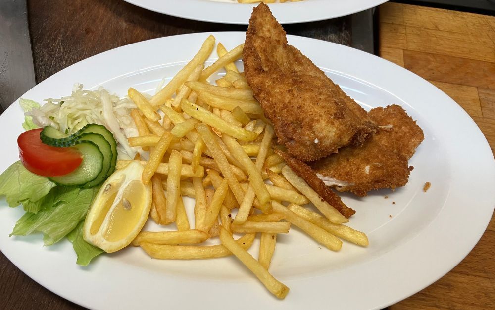 Plate with fried fish, fries, lettuce, cucumber, tomato, and lemon slice.