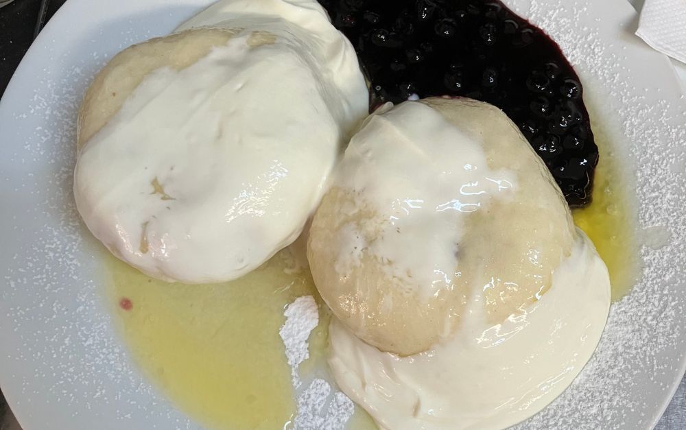 Dumplings with cream and blueberries on a white plate.