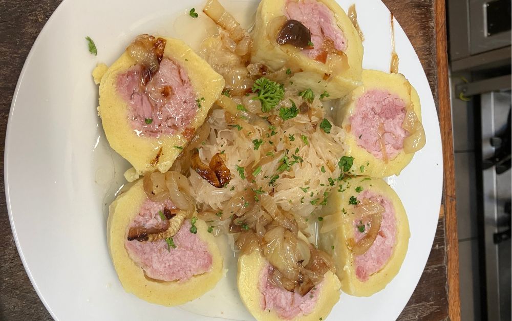 Plate of sliced dumplings with pink filling, topped with caramelized onions and parsley.