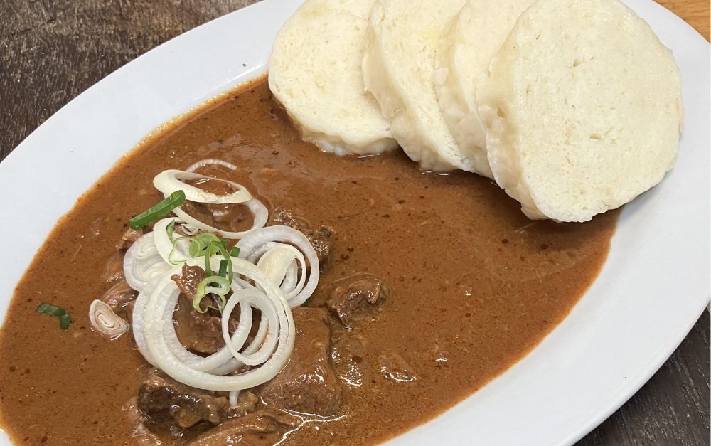 Plate with beef stew, topped with onions, and sliced bread on the side.