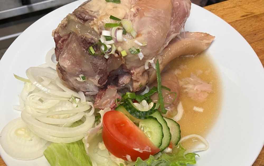 Cooked pork knuckle with sliced onions, cucumber, tomato, and lettuce on a white plate.