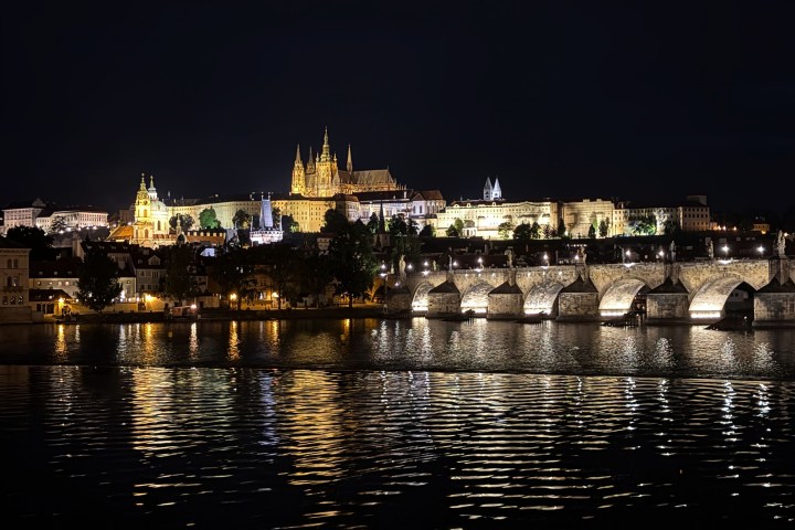 Night view of river, illuminated castle, and bridge reflections in water.
