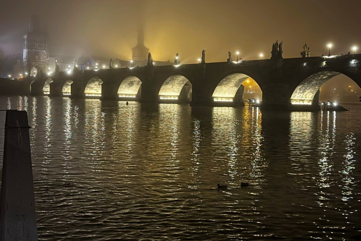 Illuminated stone bridge arches reflected in foggy river at night.
