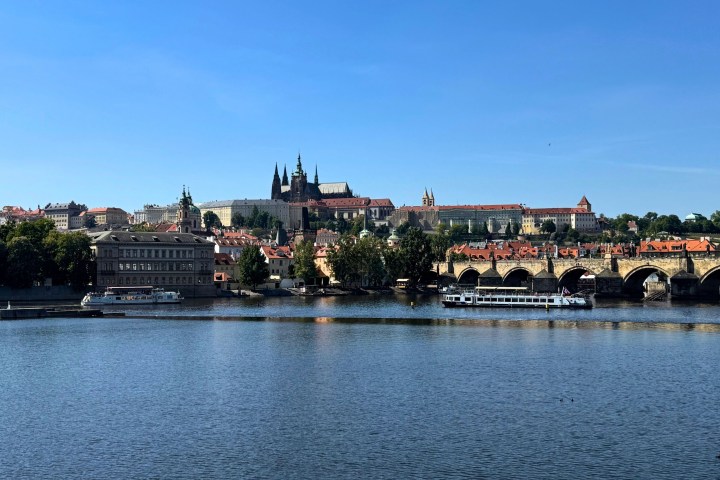 Cityscape with a river, bridge, and castle under a clear blue sky.