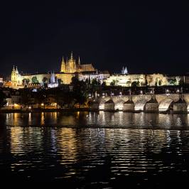 Night view of a lit castle and bridge reflecting on a river.