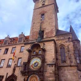 Historic clock tower with astronomical clock under cloudy sky.
