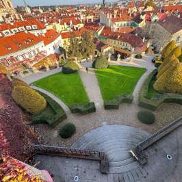 Overhead view of a garden with curved pathways and trimmed hedges, surrounded by buildings with red roofs.