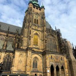Gothic cathedral with ornate facade, large stained-glass windows, people walking in front.