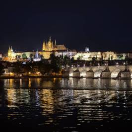 Night view of a lit-up castle and a bridge reflecting in a river.