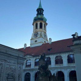 Historic church tower with clock, red roof, and ornate statues in foreground.