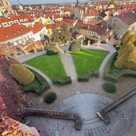 Aerial view of gardens with curved paths and circular lawn, surrounded by red-roofed buildings.